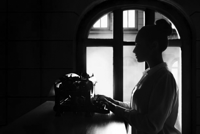 young beautiful woman author at a typewriter, writes a text, inspiration in creative work. Retro vintage typewriter side view, silhouette in a dark room against the background of a window